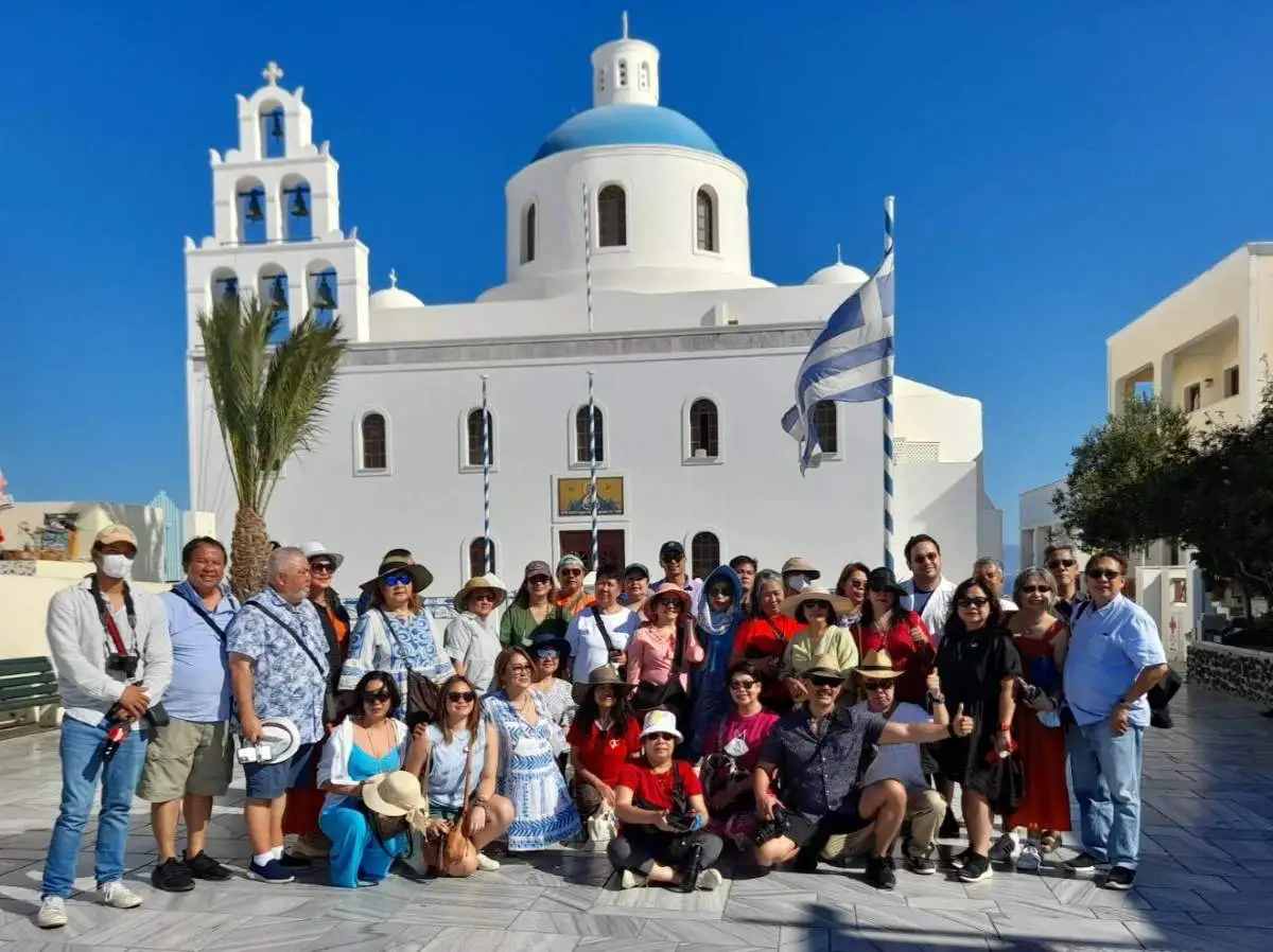 Large tour group posing in front of the iconic blue-domed church in Oia Santorini
